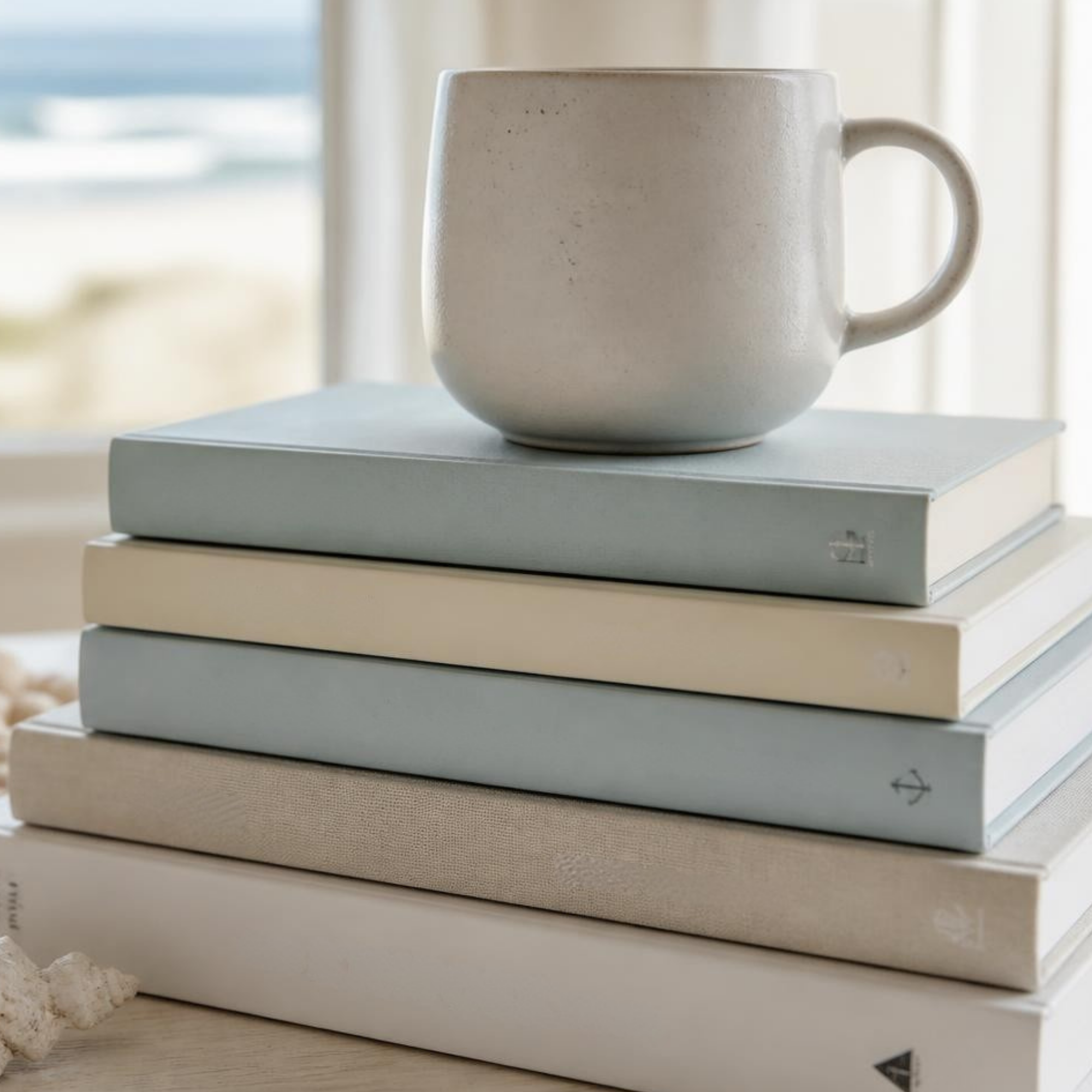 Sea-glass blue and cream books with a ceramic mug beside the ocean